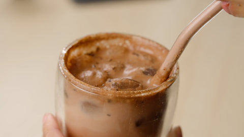 Cocoa Circle iced chocolate energy drink with cacao powder, ice cubes and straw in a glass.